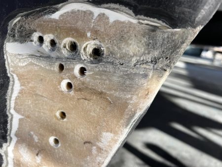 Shows holes we drilled, figuring how deep water was. Turns out keels are hollow, no real issue having water in them except it shouldn't be there. We should have started drilling lower.
Prepping Swiss cheese effect for filling with epoxy. Notice grey area where keel joins hull, quite pronounced on stern end. Effectively the glass lacks resin in original lay up, annoying but no buggy for a boat this old. Water seeped into keel here.
Note : large hole near bottom not shown, this is where the water was drained